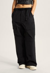 Zwarte cargobroek van een lichtgewicht stof. Kenmerken zijn een elastische tailleband met verstelbare band, zijzakken en een losse pasvorm.