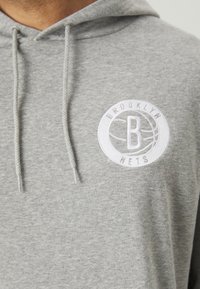 Sivi dukserica od mekanog materijala, sa bijelim izvezenim kružnim logotipom na kojem piše "BROOKLYN" i "NETS", te detaljima sa vezicama.
