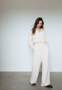 Creme oversized top med krave, parret med høj talje, brede creme bukser. Blødt stof med en glat tekstur.