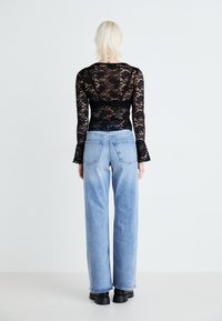 Μαύρη δαντελένια μπλούζα με μακριά μανίκια, ορατή λεπτομέρεια στην πλάτη. Ανοιχτού μπλε παντελόνι καμπάνα με κλασικές τσέπες και ξεθωριασμένο φινίρισμα. Μαύρες χοντρές μπότες.