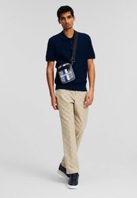 Navy polo shirt with textured knit, beige patterned pants, and navy sneakers. Includes a small black and blue crossbody bag with logo.