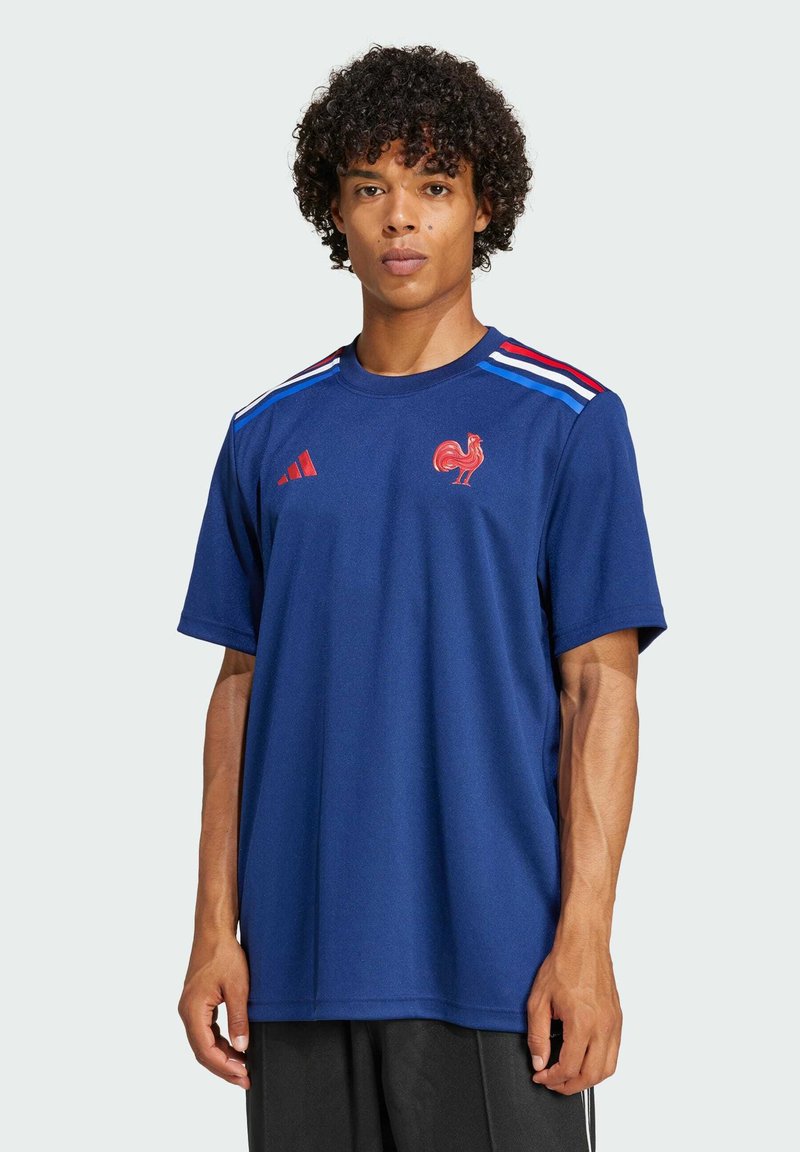 Maglietta sportiva blu marina a maniche corte, con strisce rosse e blu sulle spalle, un emblema di gallo e il logo Adidas sul petto.