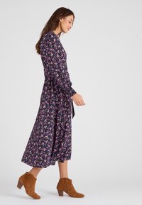 Vestido midi floral en azul marino con flores rosas y amarillas, mangas largas, detalles fruncidos en los hombros, combinado con botas de ante marrones hasta el tobillo.