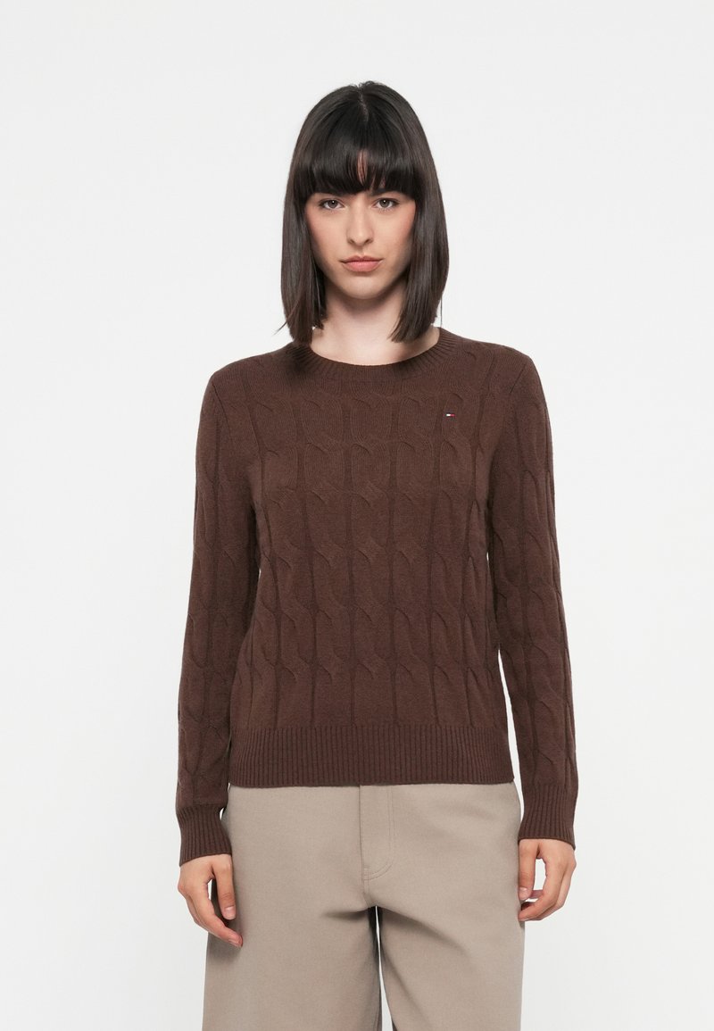 Brown knitted sweater featuring a textured cable pattern, round neck, and ribbed cuffs and hem. Subtle logo accent in the chest area.