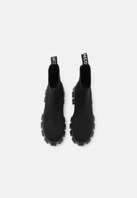 Bottines noires avec une tige en tissu texturé et une semelle en caoutchouc épaisse. Équipées de tirettes avec la marque "NCO". Design élégant et moderne.