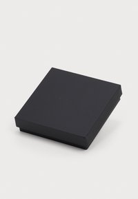 Melns kvadrāts dāvanas kastē ar smalku izspiestu logotipu uz vāka, novietots uz baltas virsmas.