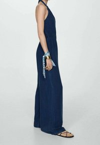 Námořnický modrý overal s halterneck výstřihem, přiléhavým korzetem a širokými kalhotami. Doplňen květinovou vzorovanou náramkem a jednoduchými sandály.