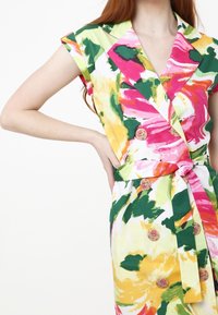 Kukallinen mekko eloisissa väreissä, joissa on keltaisia, vaaleanpunaisia ja vihreitä kuvioita. Lyhyet hihat, V-pääntie, kaksirivinen etuosa ja solmittava vyö.