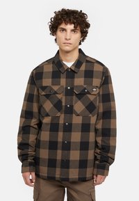 Rutig skjorta i brunt och svart, gjord av mjukt tyg. Har två bröstfickor, tryckknappar och en klassisk krage.