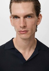 Camiseta polo de punto ribeteado en navy con cuello en V y plano, que presenta una textura suave y un ajuste a medida. Sin patrones ni adornos visibles.