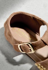 Sandale compensée en daim marron avec boucle dorée et semelle intérieure rembourrée portant l'étiquette "N. Premium Collection", vue de dessus sur une surface grise.