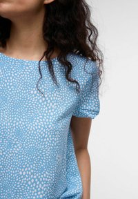 Ljusblå kortärmad topp med ett mönster av vita prickar. Mjuk tyg, rund halsringning, avslappnad passform. Lämplig för avslappnad användning.