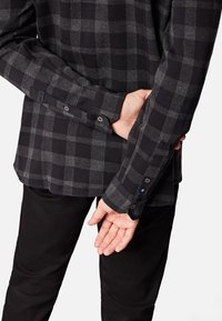 Zwarte en grijze geruite shirt met lange mouwen, knoopmanchetten, zachte stof en een gestructureerd ontwerp. Draagt met zwarte broek, waarbij de manchet details zichtbaar zijn.