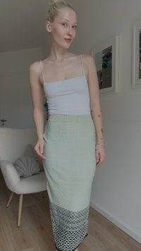 Jupe texturée de couleur vert clair, longueur genoux, avec une ceinture côtelée et un motif inférieur semblable à de la dentelle, associée à un débardeur blanc moulant.