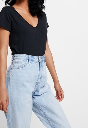 Woman wearing a black V-neck T-shirt tucked into high-waisted light blue denim jeans against a plain white background.