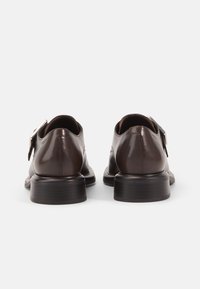 Brown leather shoes with a smooth finish, featuring a buckle strap, rounded toe, and a stacked heel. Subtle stitching detail on the sides.
