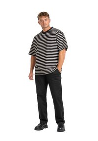 Camisa de manga corta a rayas negras y crema con escote en V, combinada con pantalones negros y zapatos gruesos negros. Diseño simple y de corte relajado.