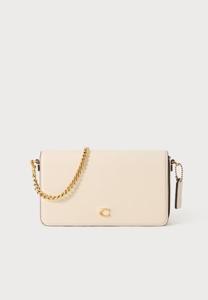 Cream-colored leather crossbody bag with a gold chain strap and logo accent. Features a textured finish and a side tag detail.