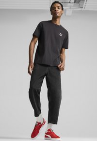 Sort bomuld t-shirt med et lille hvidt logo, parret med flagrende sorte denim jeans og røde ruskind sneakers med hvide såler.