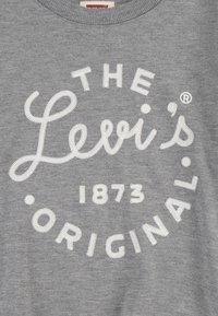 Sudadera gris con texto bordado blanco que dice "THE Levi's 1873 ORIGINAL" en un diseño circular. Textura de tela suave.