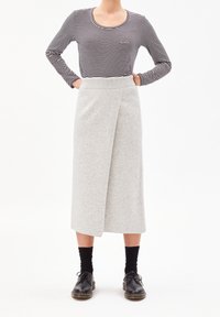 Maglia a maniche lunghe a righe abbinata a una gonna avvolgente grigia al ginocchio. L'outfit presenta un cinturino a costine e scarpe nere con lacci.