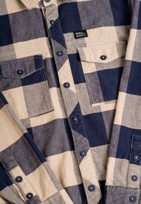 Camisa de franela a cuadros en beige y azul marino que cuenta con dos bolsillos en el pecho, cierre de botones en la parte delantera y botones en contraste. Mezcla de algodón, textura de peso medio.