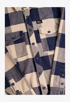 Camisa de franela a cuadros en beige y azul marino que cuenta con dos bolsillos en el pecho, cierre de botones en la parte delantera y botones en contraste. Mezcla de algodón, textura de peso medio.