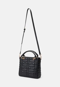 Sac à main noir matelassé en cuir, doté d'une forme structurée, de poignées supérieures et d'une bandoulière amovible et ajustable avec des accessoires en ton doré.