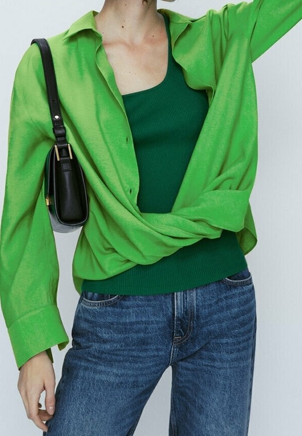 Personne portant une chemise boutonnée vert vif nouée à la taille, un débardeur vert foncé, un jean bleu et un sac à bandoulière noir.