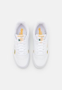 Ett par vita Reebok Classic vegan sneakers med gula och gröna accenter, sedda ovanifrån på en vit bakgrund.