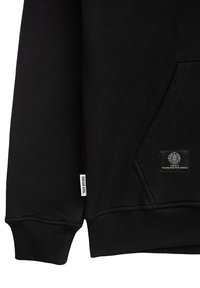 Svart sweatshirt i teksturert stoff, med en frontlomme, ribbestrikkede mansjetter og to vevde merker med merkevare og et grafisk logo-patch.