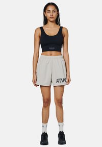 Svart crop top med "HALO"-logotyp, beige shorts med "ATW"-tryck, bärs med svarta sneakers och vita strumpor. Slät tyg, avslappnad passform.