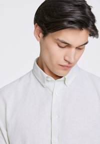 Ljusgrön linne skjorta med knapp längst fram, spetsad krage och subtil textur; har vita knappar fram.