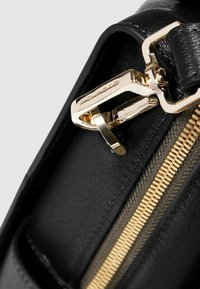 Zwarte leren tas met een gouden ritssluiting en hardware. Close-up van de ritstrekkker en details, met een gladde textuur en stiksels.