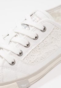 Baskets blanches avec un motif de lacets texturés sur le côté, semelle en caoutchouc et lacets blancs. Œillets métalliques pour les lacets ajoutant une touche de détail.