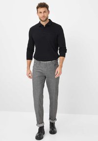Zwarte langegemouwen poloshirt met een borstzak, gecombineerd met grijs heather slim-fit broek, opgerolde mouwen en zwarte veterschoenen.