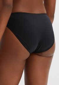 Culotte taille haute noire en tissu lisse, avec un délicat bord festonné le long de la taille et des ouvertures de jambes pour un look ajusté.