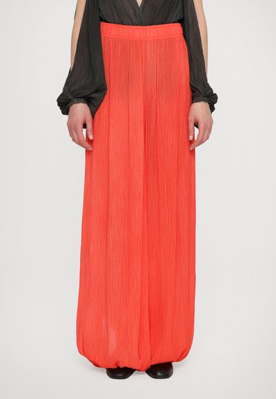 Pantalons amples plissés orange vif avec une finition texturée, dotés d'une taille à cordon et d'un ajustement confortable, associés à un haut sombre.