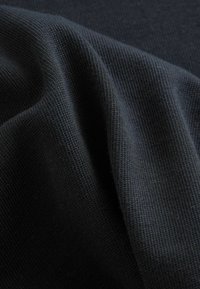 Tela negra con una superficie suave y texturizada, con patrones de punto consistentes, drapeada suavemente para mostrar profundidad y pliegues.