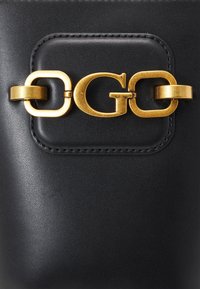 Černá kožená taštička s hladkým povrchem, s uzávěrem ve zlatém tónu a s embosovaným logem uprostřed.