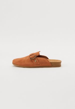 Sapatos slip-on de camurça castanha com biqueira arredondada, apresentando um detalhe de fivela lateral e uma palmilha texturizada de cortiça natural.