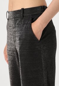 Pantalons tissés noirs avec un éclat métallique texturé, dotés d'une pochette latérale et d'une coupe ajustée à la taille.