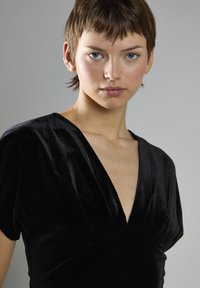 Czarna aksamitna sukienka z głębokim dekoltem w kształcie litery V, krótkimi rękawami i usztywnioną górą. Gładka tekstura i subtelny połysk podkreślają design.