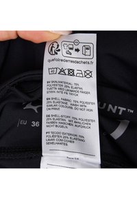 Sort stofmærkat der detaljerer materialets sammensætning: 75% polyester, 25% elastan. Flere sprog og vaskeanvisninger vises.