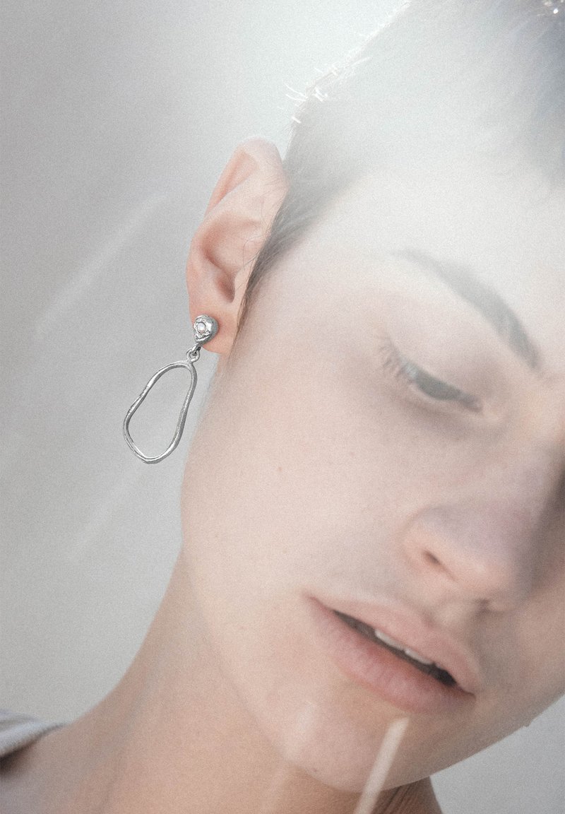 Hõbedased tilga kõrvarõngad on ebaregulaarse, pikliku kujuga, millel on poleeritud viimistlus ja väike ringikujuline nupuke. Tekstureeritud pind lisab visuaalset huvi.