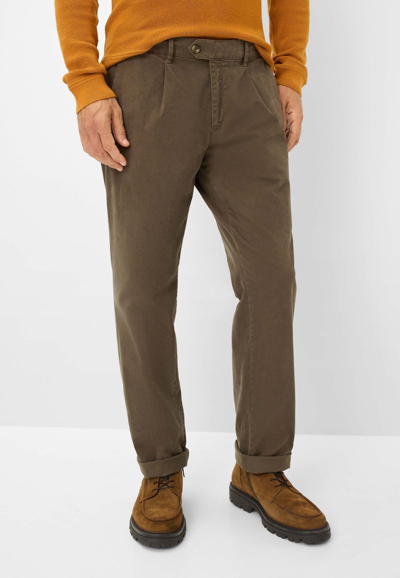 Bruine katoenen broeken met een rechte pasvorm, voorzien van een knoopsluiting en opgerolde mouwen. Gemaakt in combinatie met bruine suède schoenen.