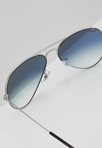 Silver metal aviator sunglasses with gradient blue lenses, featuring adjustable nose pads and thin black temple tips.