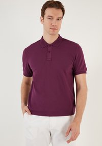 Poloko s krátkým rukávem v tmavě fialové barvě, vyrobené z hladkého materiálu. Má třídobrou knoflíkovou légou a žebrovaný límec. Nosit s bílými kalhotami.