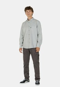 Hellgrau karierter Button-Up-Hemd mit einer Tasche, kombiniert mit dunkelgrauenCargo-Hosen und schwarzen Sneakers mit weißen Sohlen.