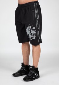 Zwarte sportshorts van een geweven stof, met een grijze grafische print en zijbranding. Gepaard met zwarte hoge sneakers.